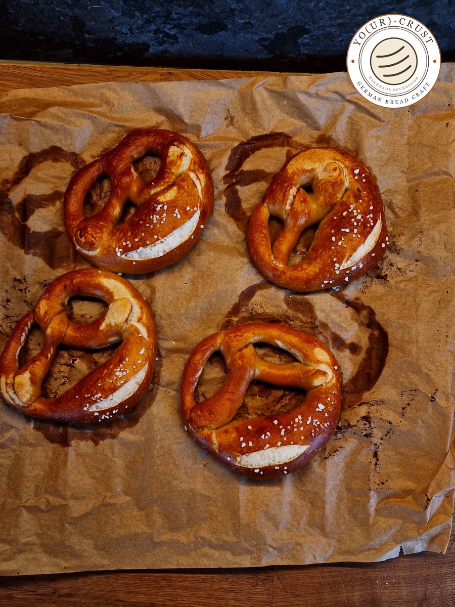 24-Hour Swabian Sourdough Pretzels — four glossy dark brown lye pretzels with coarse salt on baking paper